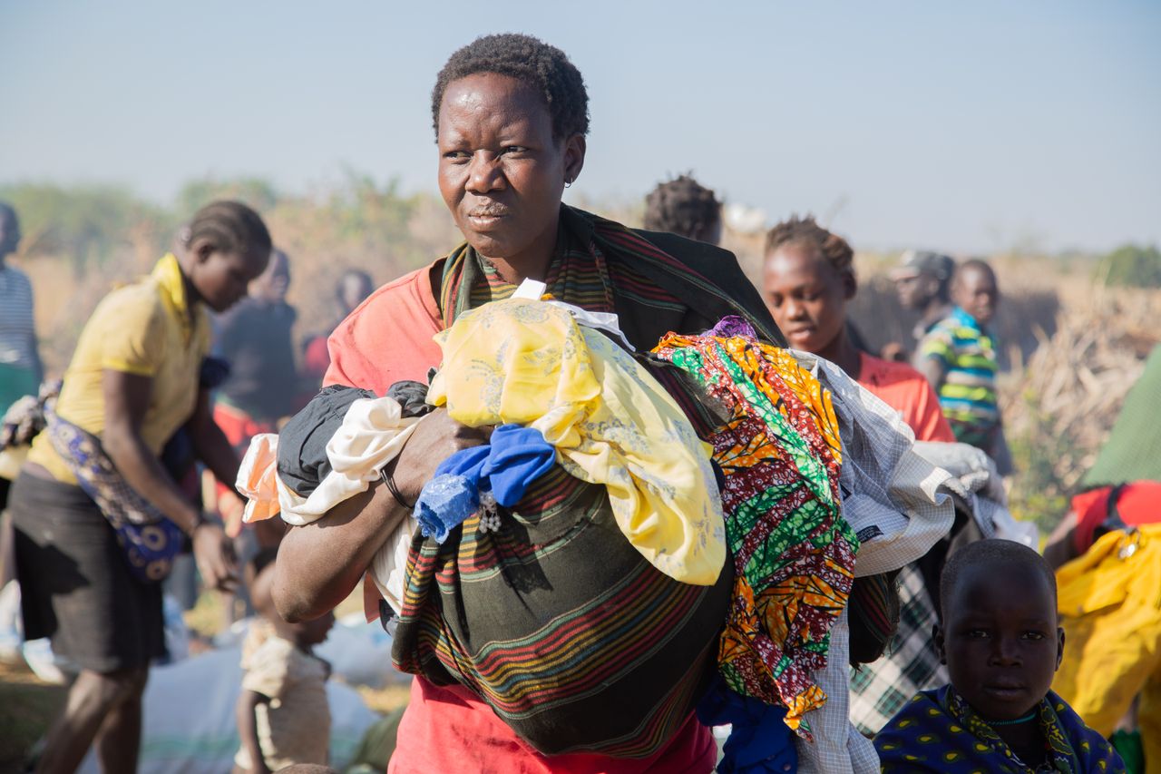 A group of African women and children at an outdoor community gathering on a sunny day.