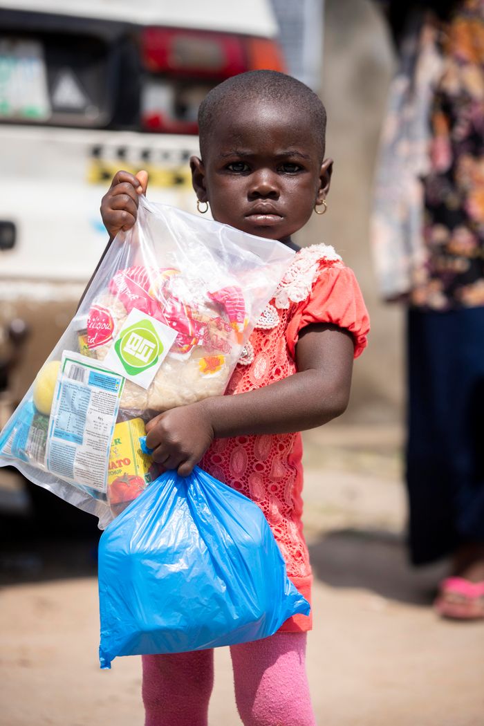 services-01 A young African girl holding relief supplies in plastic bags outdoors.