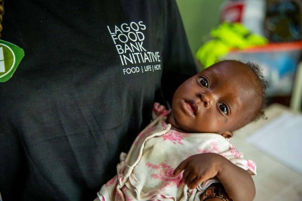 why-choose-us-02 A compassionate volunteer holds a baby at the Lagos Food Bank to support vulnerable children.